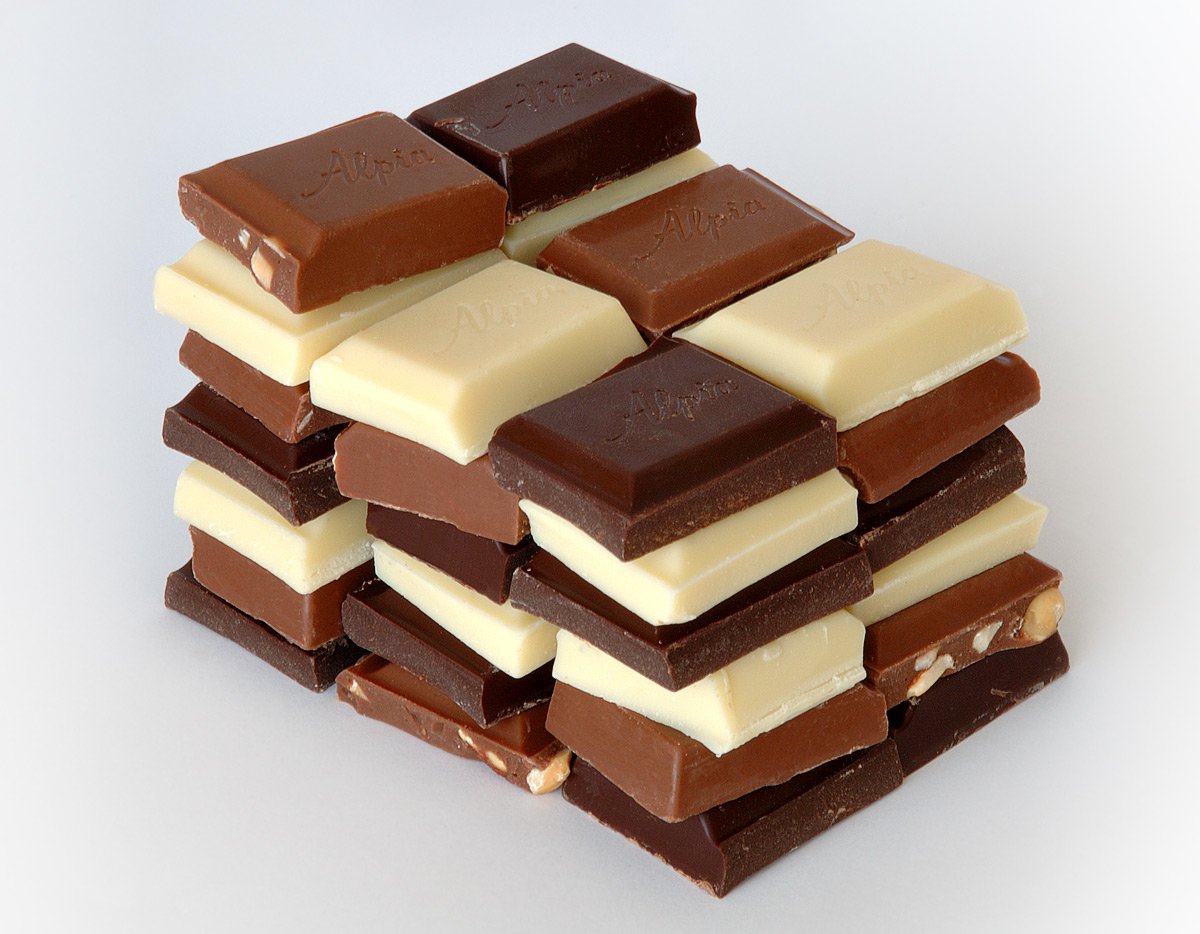 A stack of various chocolate bars, including dark, milk, and white chocolate, arranged neatly on a light background, showcasing a delicious assortment of sweets.