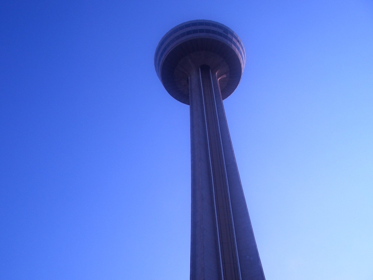 A tall man-made tower building extends upward against a clear blue sky.
