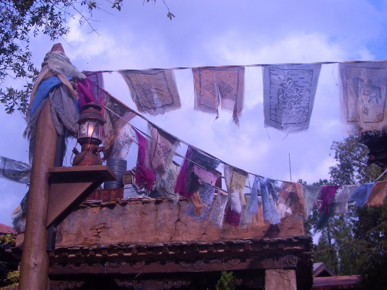 A row of colorful flags hangs above a rustic wooden structure under a clear blue sky.