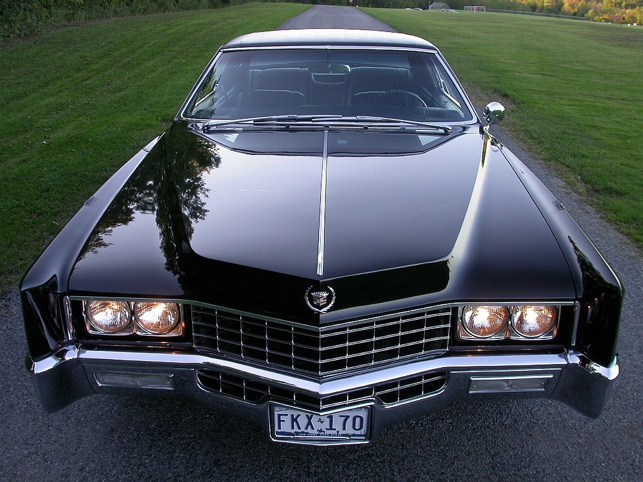 Front view of a black Cadillac Eldorado parked on a road with grass on both sides, showcasing its distinctive grille and quad headlights.