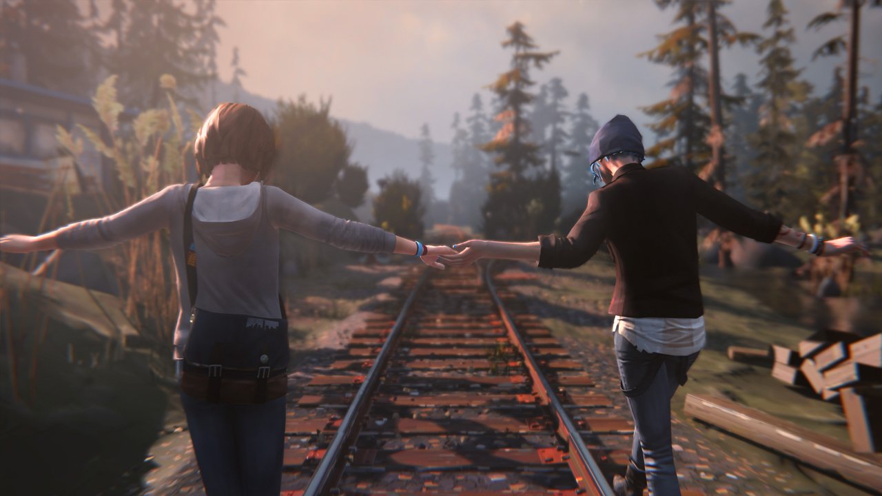 Two characters from the video game Life Is Strange balance hand-in-hand on rusty train tracks at sunset, one wearing a blue beanie.