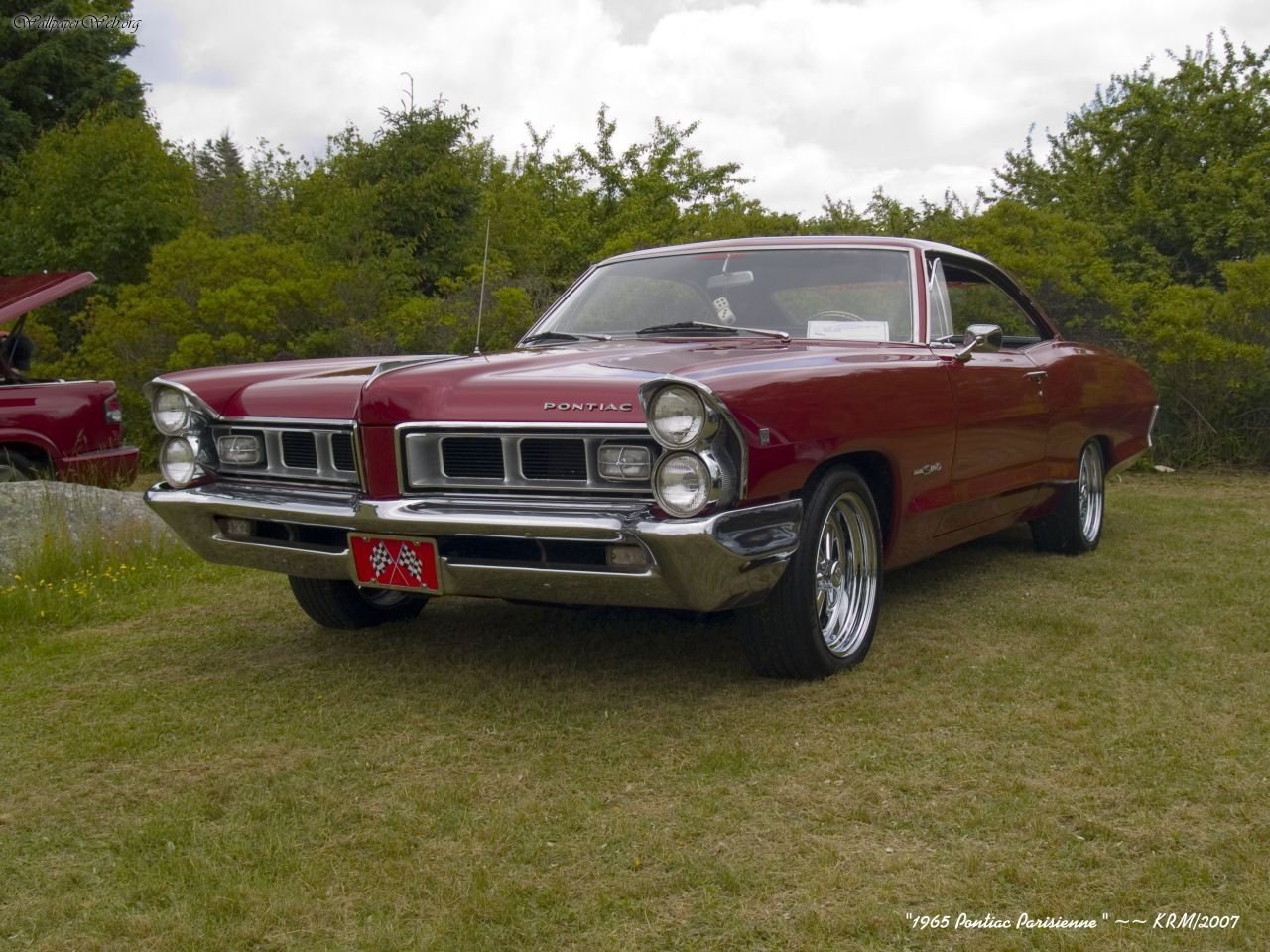 Maroon Pontiac Parisienne vehicle parked on grass, shown in a front three-quarter view with chrome grille and wheels.