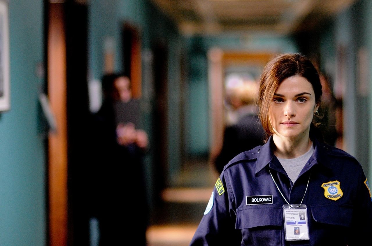 Woman in a security uniform with badge and ID standing in a corridor, facing the camera — scene from the movie The Whistleblower.