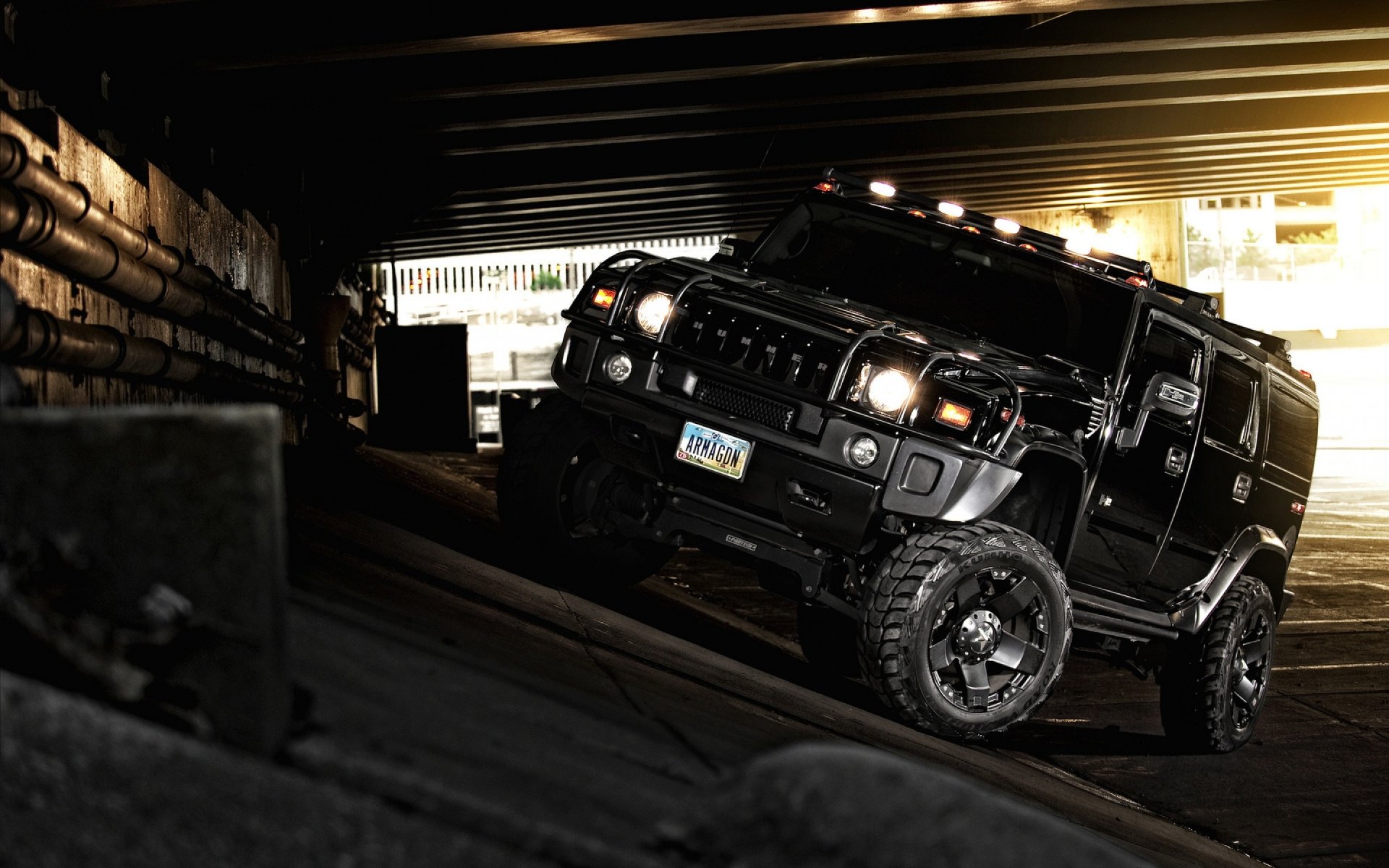 A black Hummer maneuvers through a dimly lit underpass, showcasing its rugged design and off-road capabilities against an industrial backdrop.