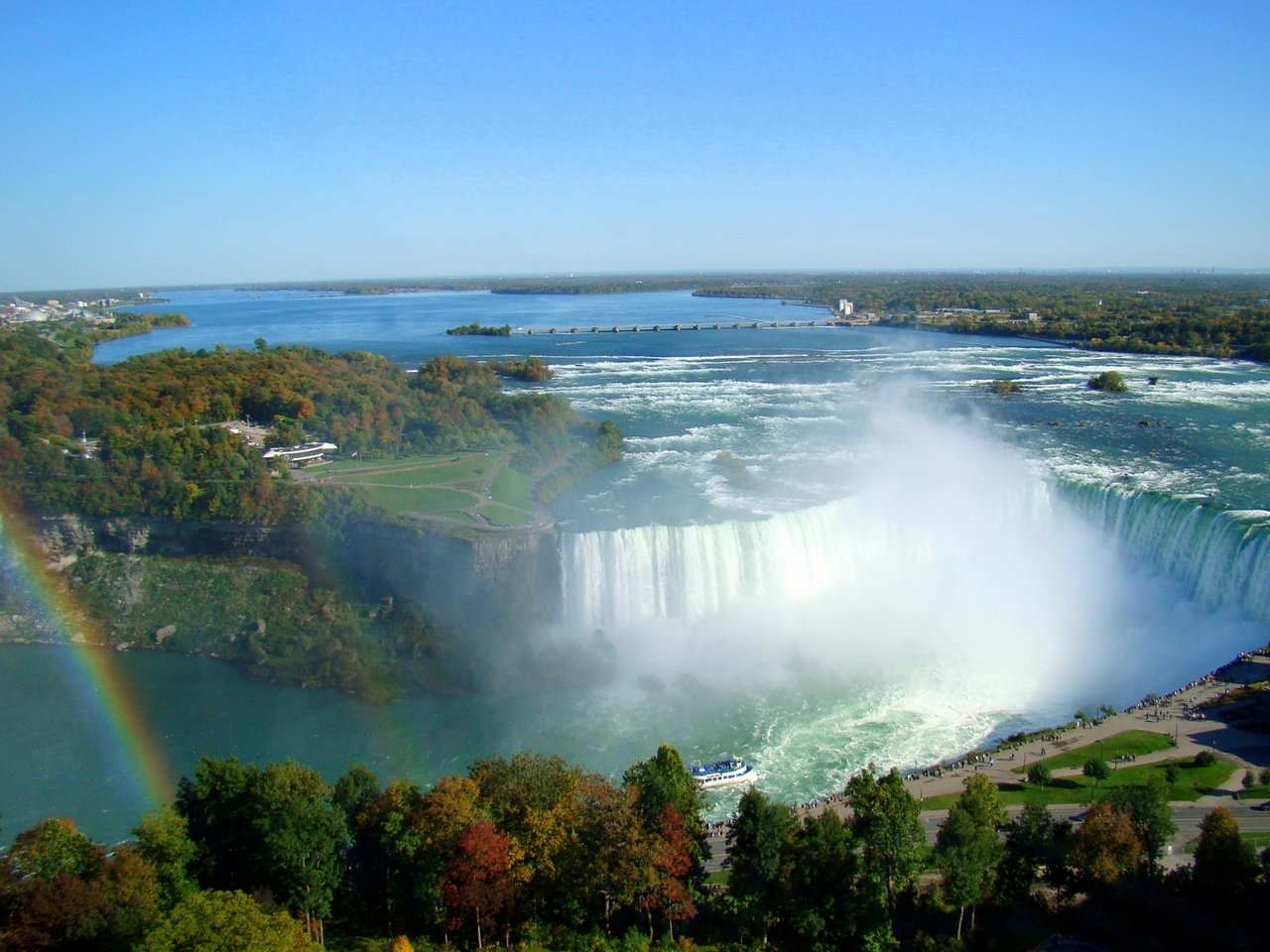 A stunning view of Niagara Falls surrounded by lush greenery and water mist, showcasing the powerful cascade and the vibrant landscape of nature.