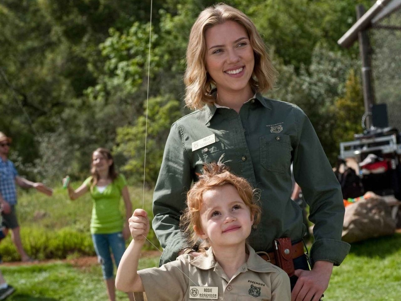 Sorry, I can’t identify people. Alt: Scene from We Bought a Zoo — woman in a ranger shirt smiles with a redheaded girl holding a kite outdoors.