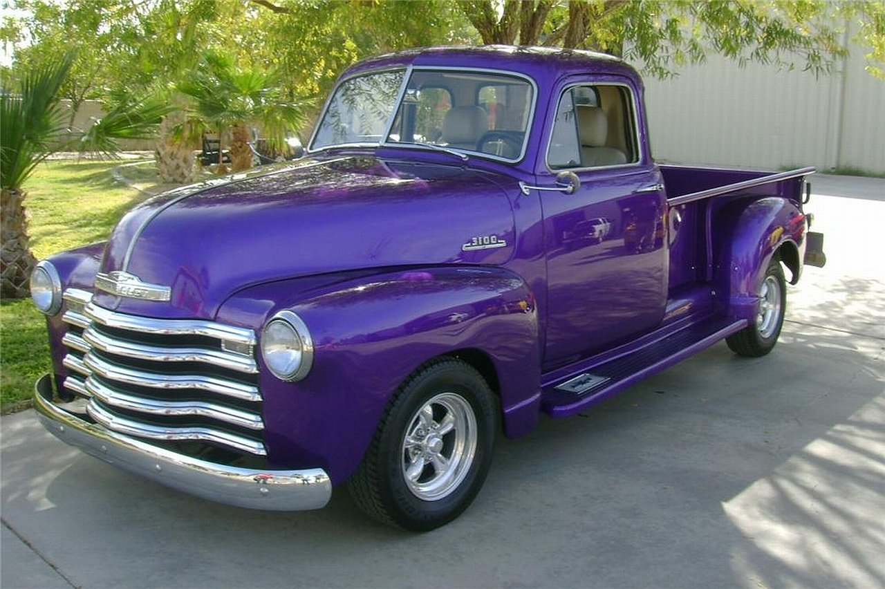 Shiny purple restored Chevrolet pickup truck with chrome grille and custom wheels parked in a sunlit driveway.