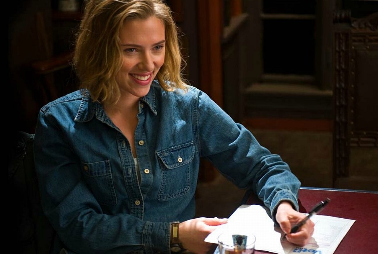 Scarlett Johansson smiles while writing at a table in a scene from the movie We Bought A Zoo.