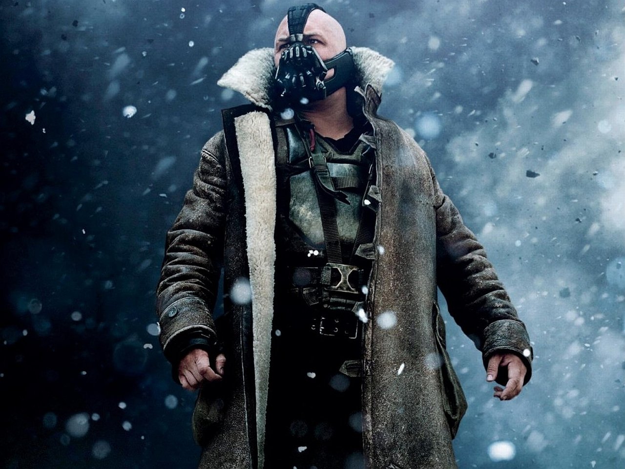 Bane from DC Comics stands defiantly in the snow, wearing a heavy fur-lined coat, as seen in the movie The Dark Knight Rises.