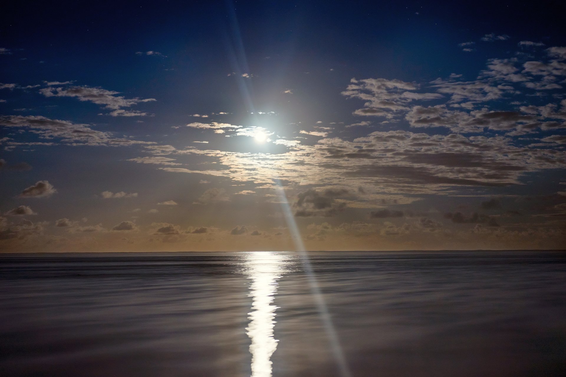 Moonlit scene over Mauritius: the moon casts a bright silvery path across the calm ocean, framed by scattered clouds and a deep night sky.
