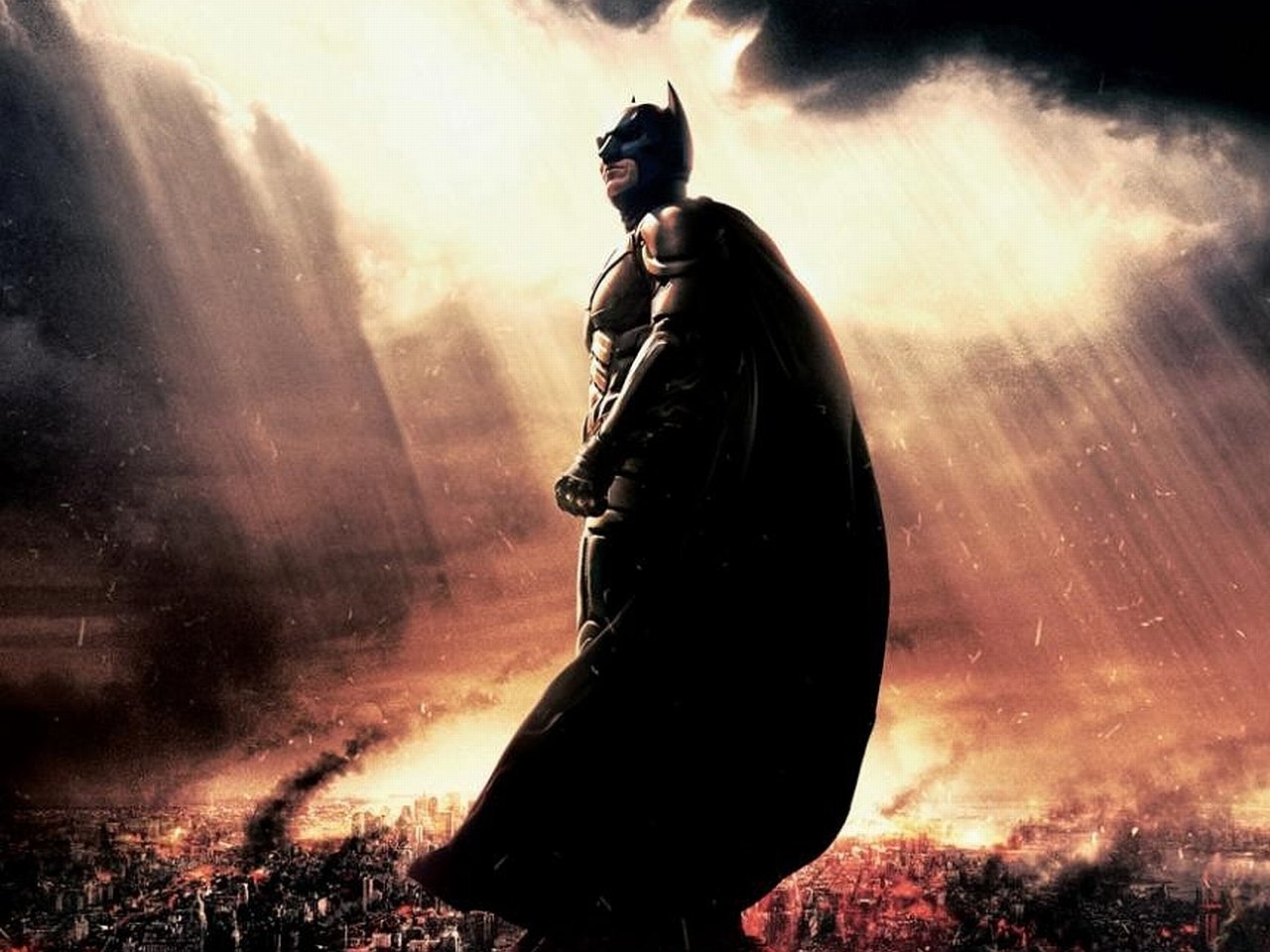 A dramatic scene from *The Dark Knight Rises*, featuring Batman standing resolutely against a backdrop of chaos and striking beams of light breaking through dark clouds.