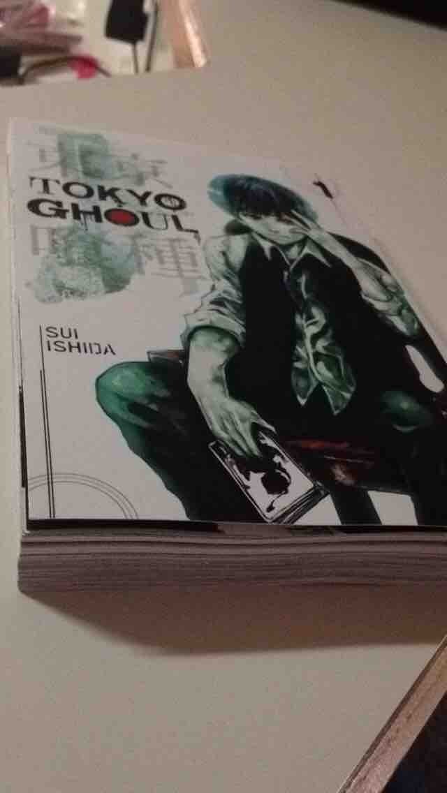 Anime — Tokyo Ghoul manga volume on a table, cover art by Sui Ishida showing dark-haired Kaneki seated in a shirt and loosened tie, holding a card/book.