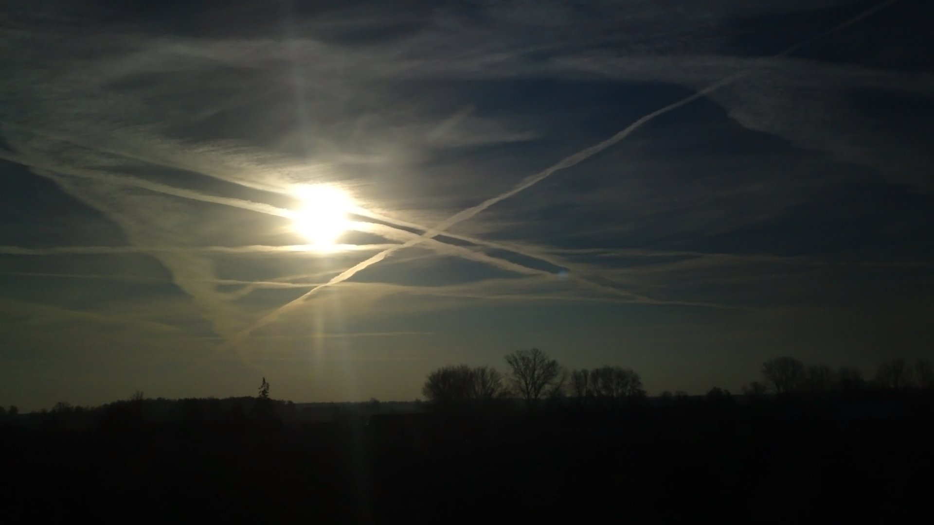Sunset with scattered clouds creating streaks across the sky above a darkened natural landscape.