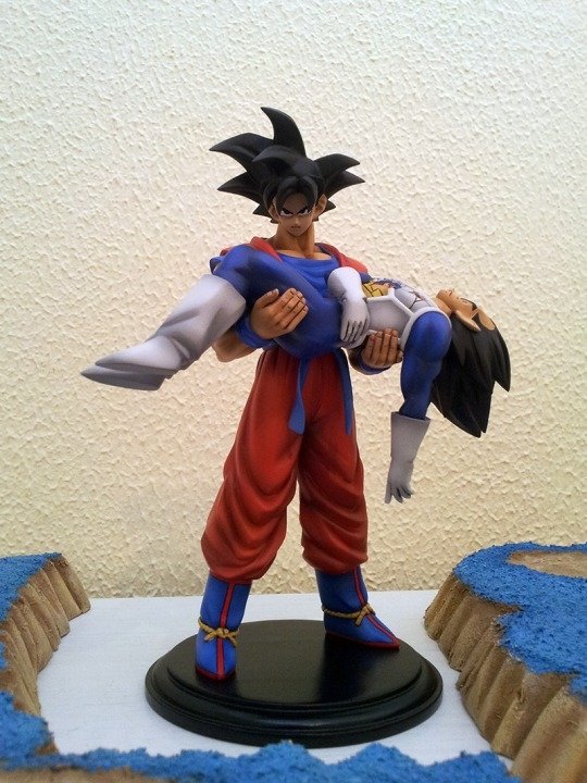 A detailed anime figure from Dragon Ball Z features a character in orange and blue attire, holding another character in a dramatic pose, set on a stylized base.