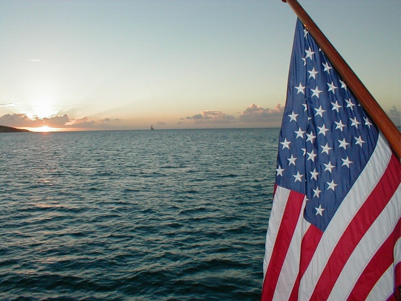 An American flag waves proudly against a serene sunset over the ocean, capturing a moment of tranquility and patriotism against the vast waters.