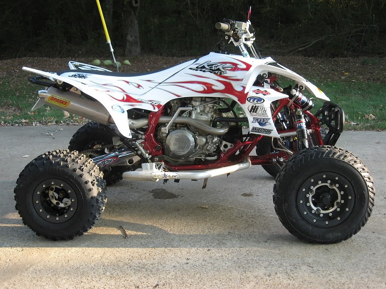 White Yamaha YFZ 450 quad with red frame and flame graphics, knobby off-road tires and aftermarket exhaust parked on pavement against a wooded background.