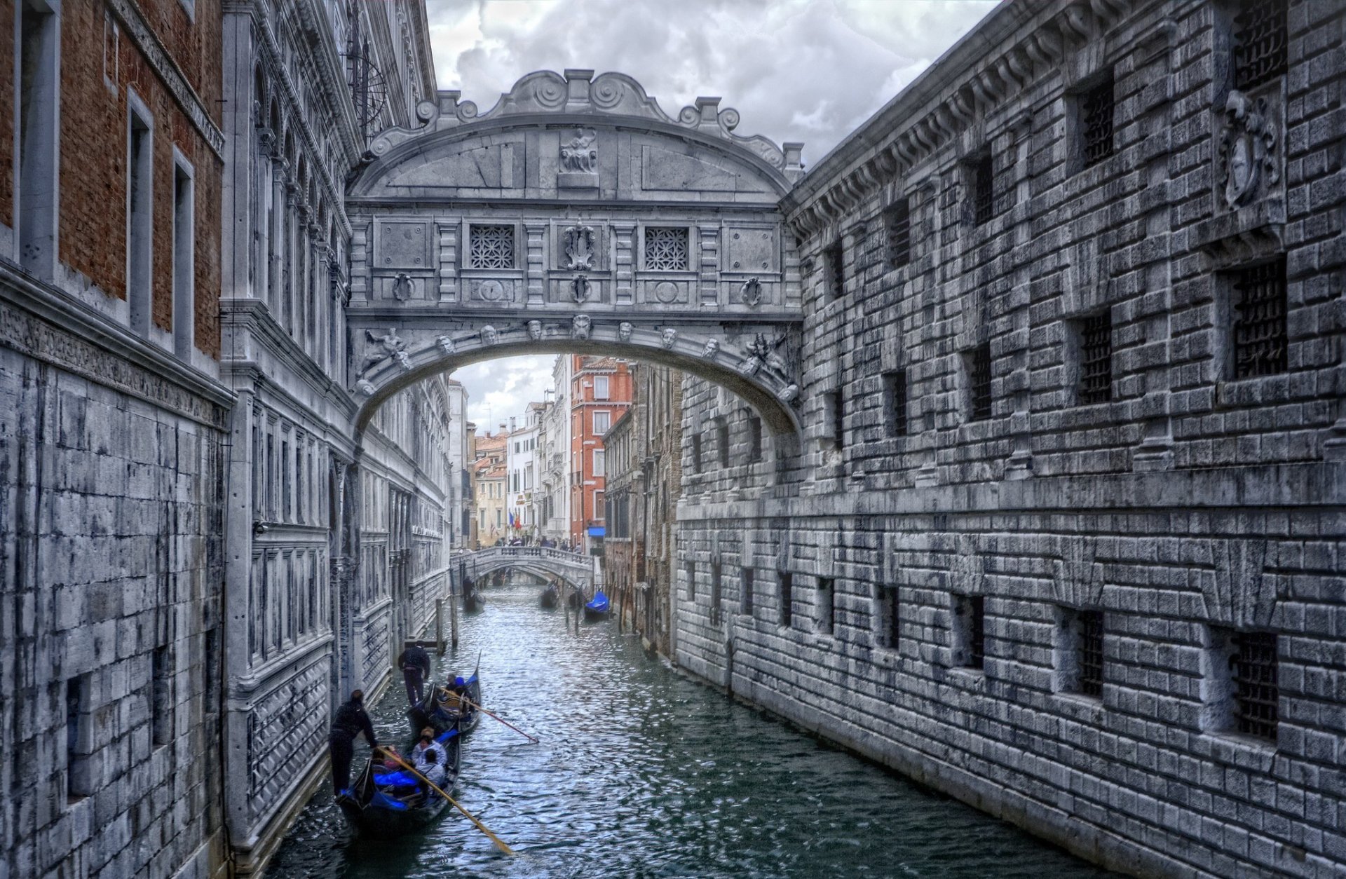 View under the Bridge of Sighs in Venice, Italy: enclosed stone bridge spanning a narrow canal with gondolas and historic man-made palazzi lining the water.