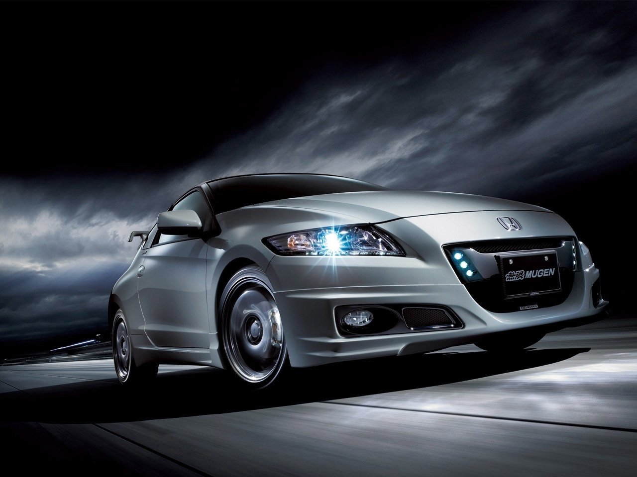 Silver Honda CR-Z vehicle driving at speed with headlights and LED accents glowing against a dramatic stormy sky.