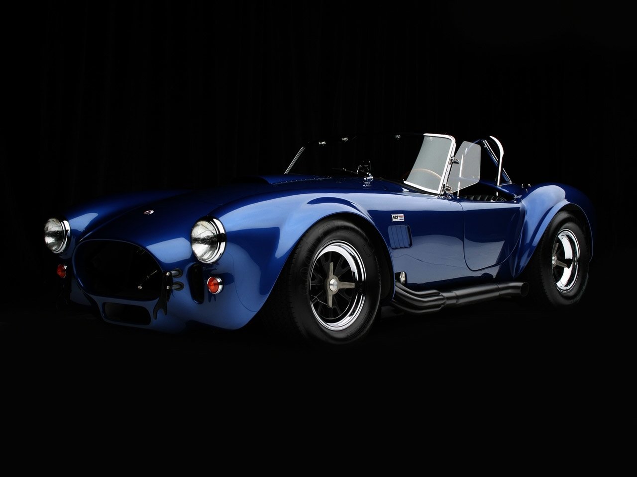 Blue AC Cobra vehicle showcased against a black background, highlighting its sleek, classic roadster design and distinctive curves.