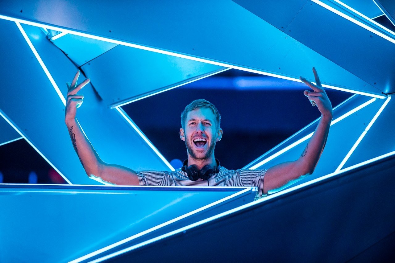 A DJ performs surrounded by vibrant blue lighting, energetically engaging the audience. This scene captures the essence of Calvin Harris's dynamic music style.