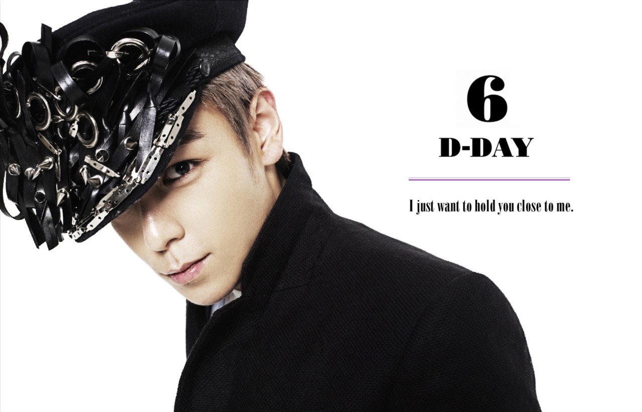A stylish member of Bigbang wears a striking hat and a black coat, looking directly at the camera with a heartfelt message: I just want to hold you close to me. D-DAY countdown.
