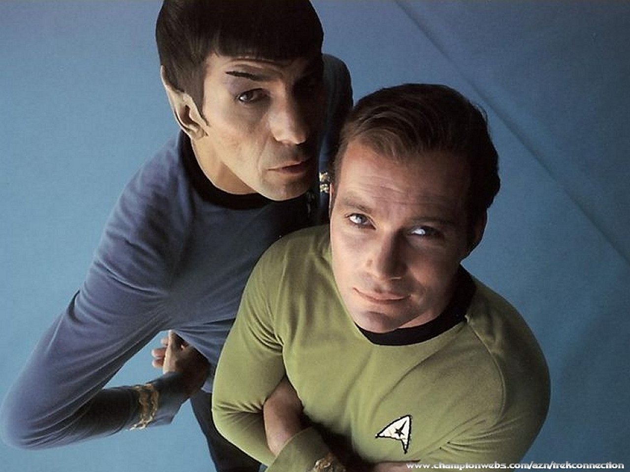 Spock and Captain Kirk from the TV show Star Trek: The Original Series stand together, with Spock leaning closely behind Kirk.