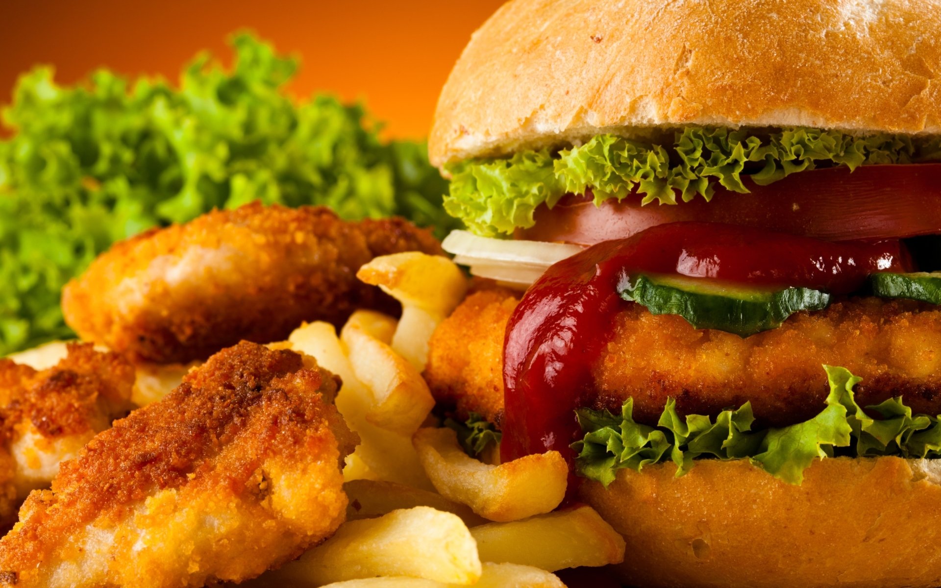 A close-up of a crispy chicken burger with lettuce and ketchup, accompanied by French fries and chicken nuggets, against a vibrant orange background.