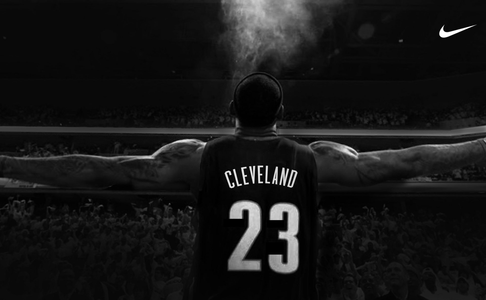 Back view of a Cleveland Cavaliers basketball player wearing #23 with arms outstretched under arena lights; Nike swoosh visible on the upper right.