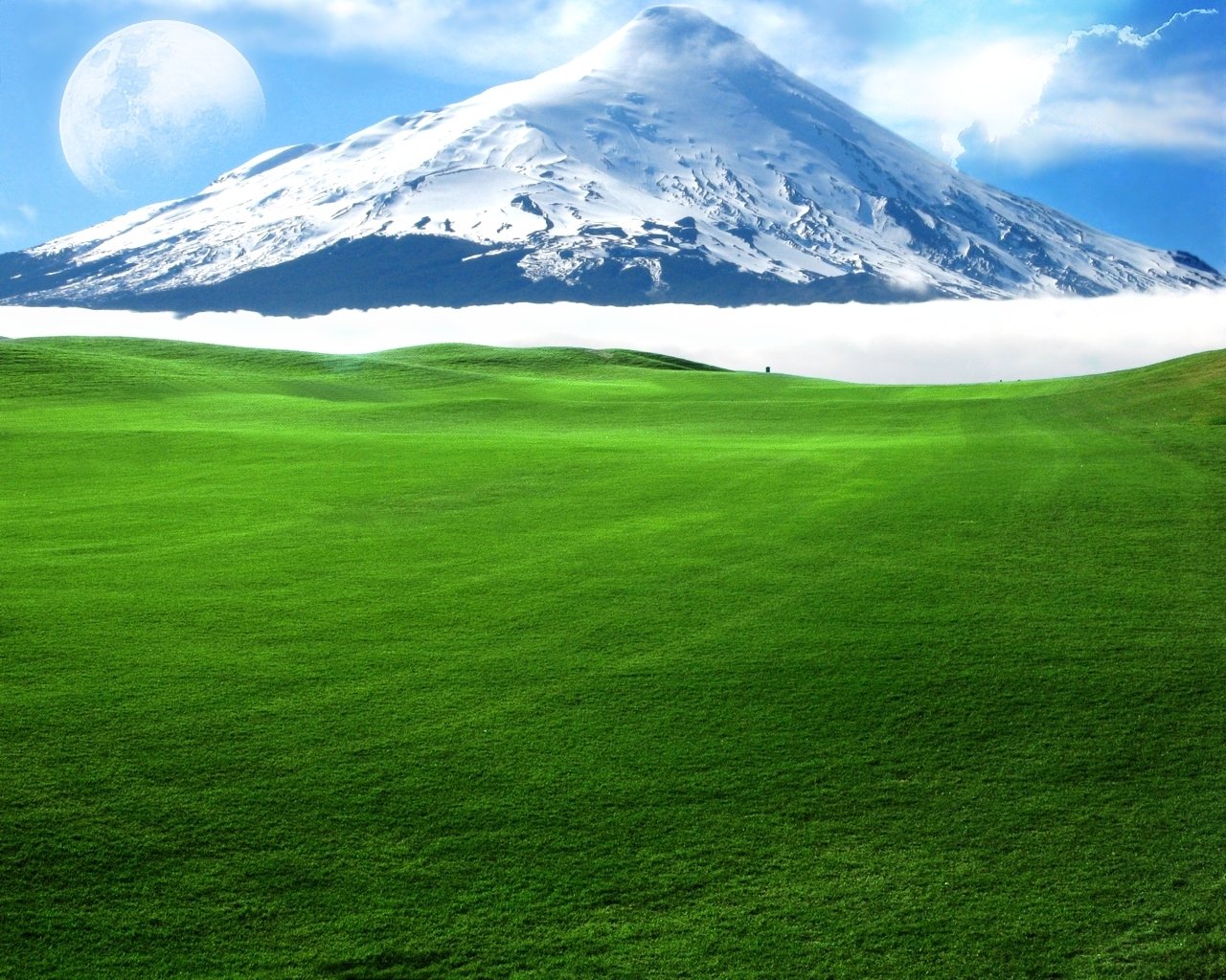 A lush green field stretches towards majestic mountains topped with snow, under a dreamy sky that enhances the natural beauty of this serene landscape.