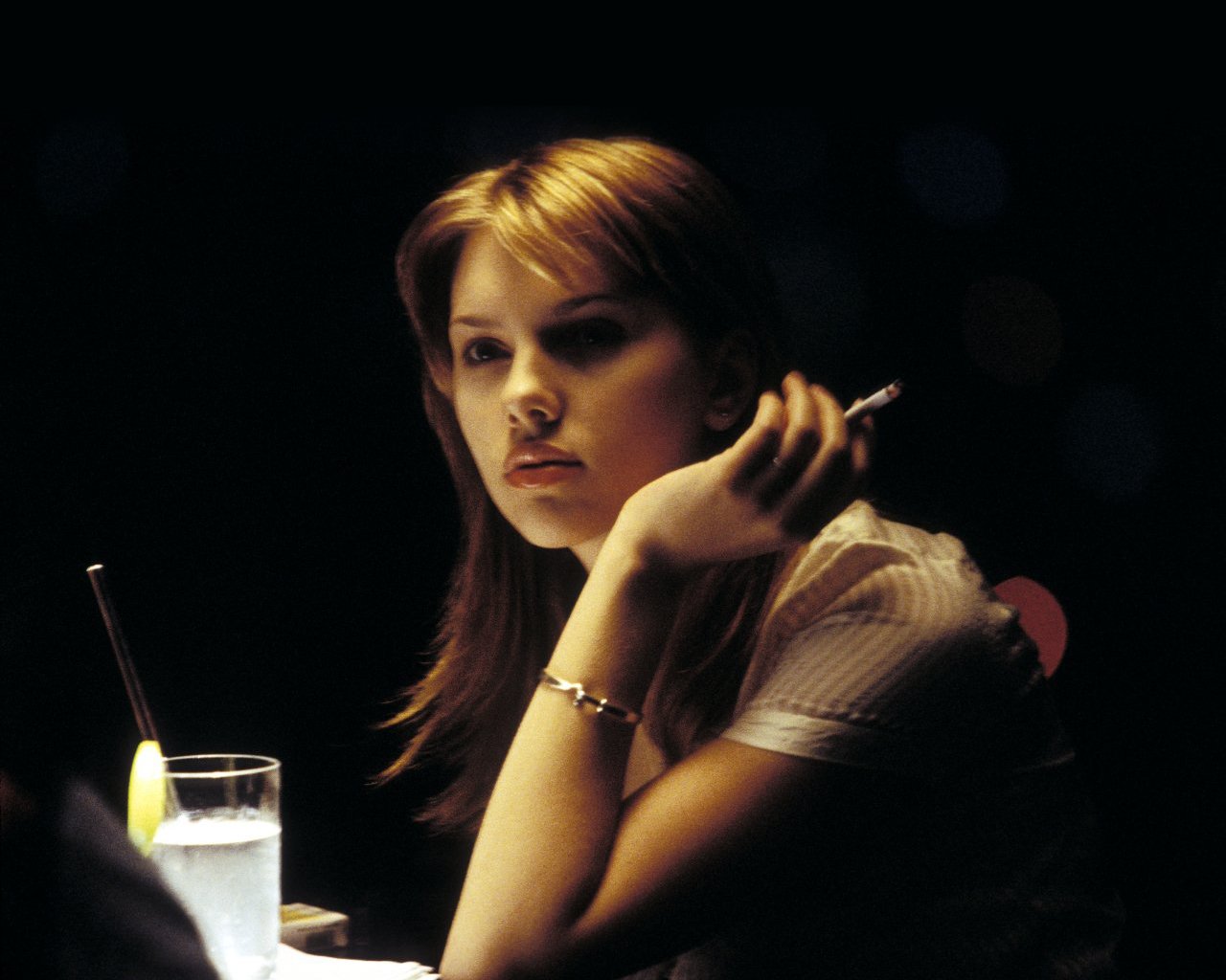 Scarlett Johansson in a moody scene from the movie Lost in Translation, sitting at a bar with a drink and a contemplative expression.