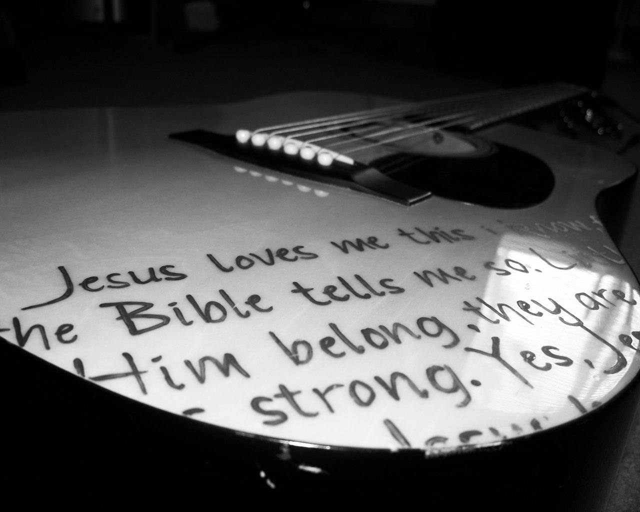 An acoustic guitar with handwritten lyrics from Jesus Loves Me on its body, showcasing a blend of music and personal expression.