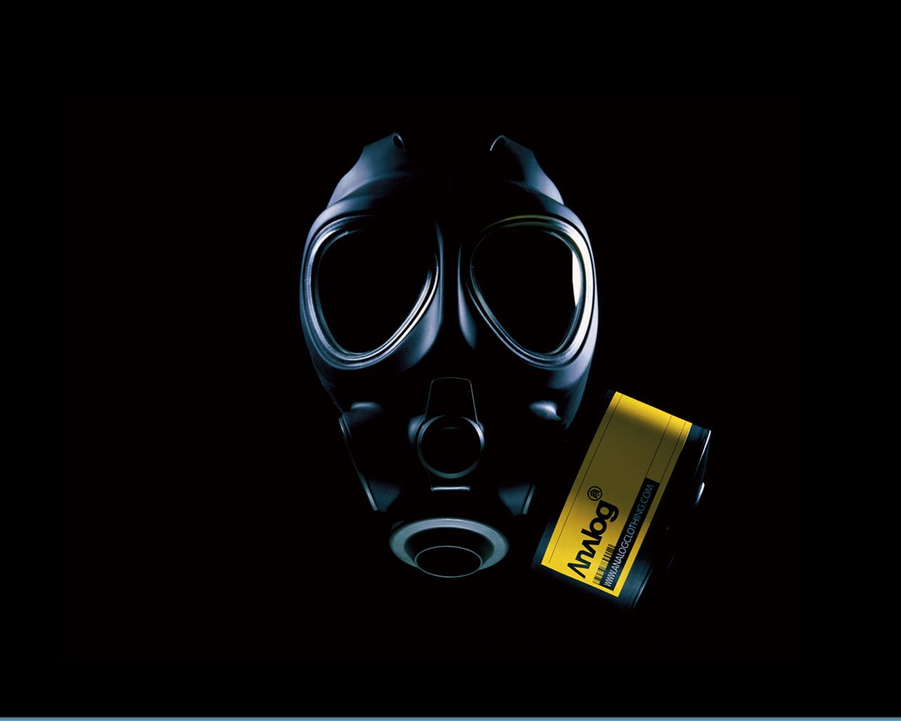 A dark image featuring a gas mask in the foreground, emphasizing its contours, with a yellow canister positioned beside it. The overall atmosphere is mysterious and intense.