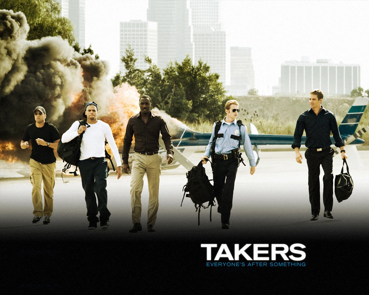 Promotional image for the movie Takers showing five characters confidently walking away from a smoky explosion with a city skyline in the background.