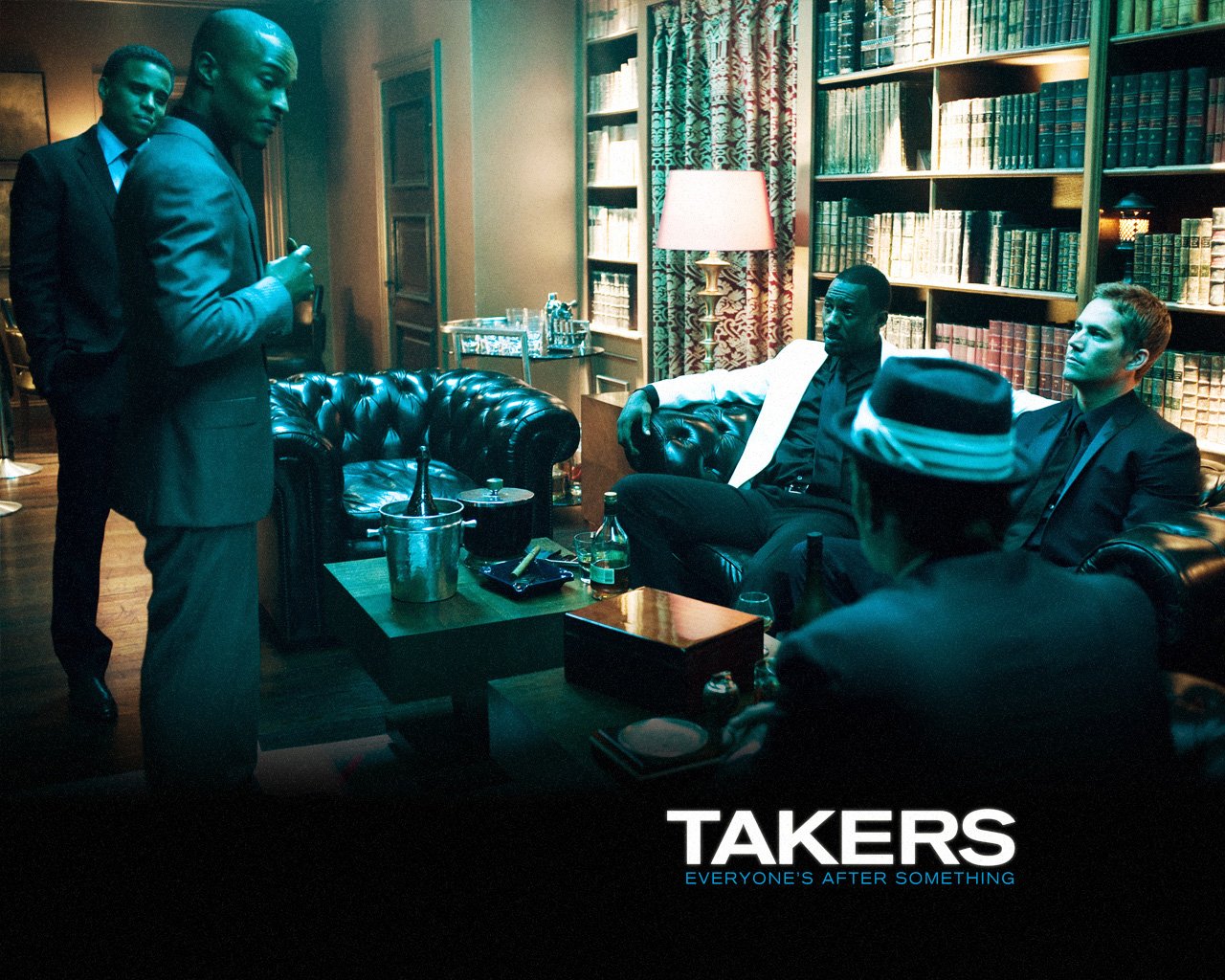 Scene from the movie Takers featuring five men in a dimly lit room with bookshelves, leather couches, and a table with drinks.