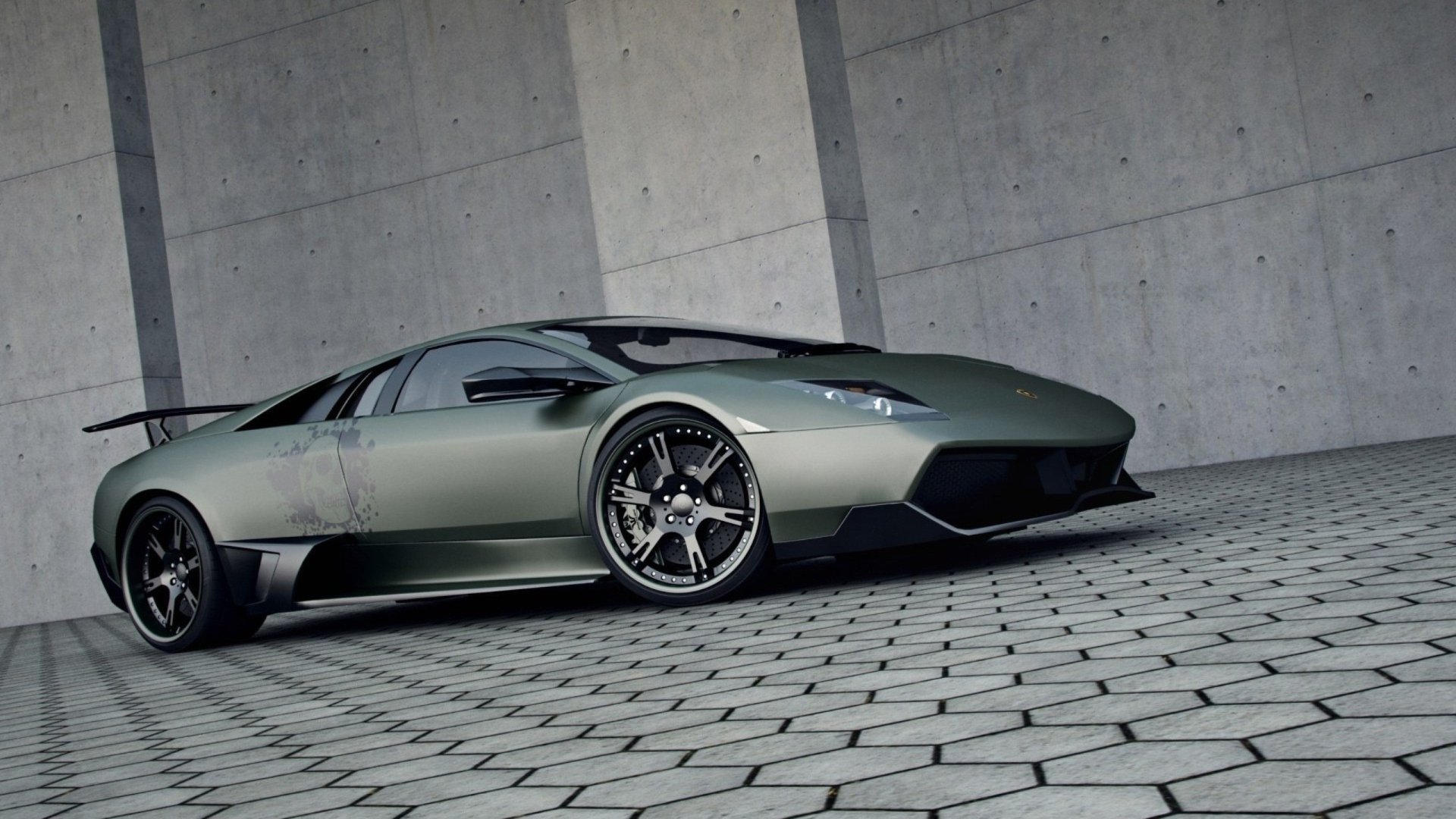 A sleek Lamborghini Murcielago sports car parked on a patterned pavement in front of a modern concrete wall.