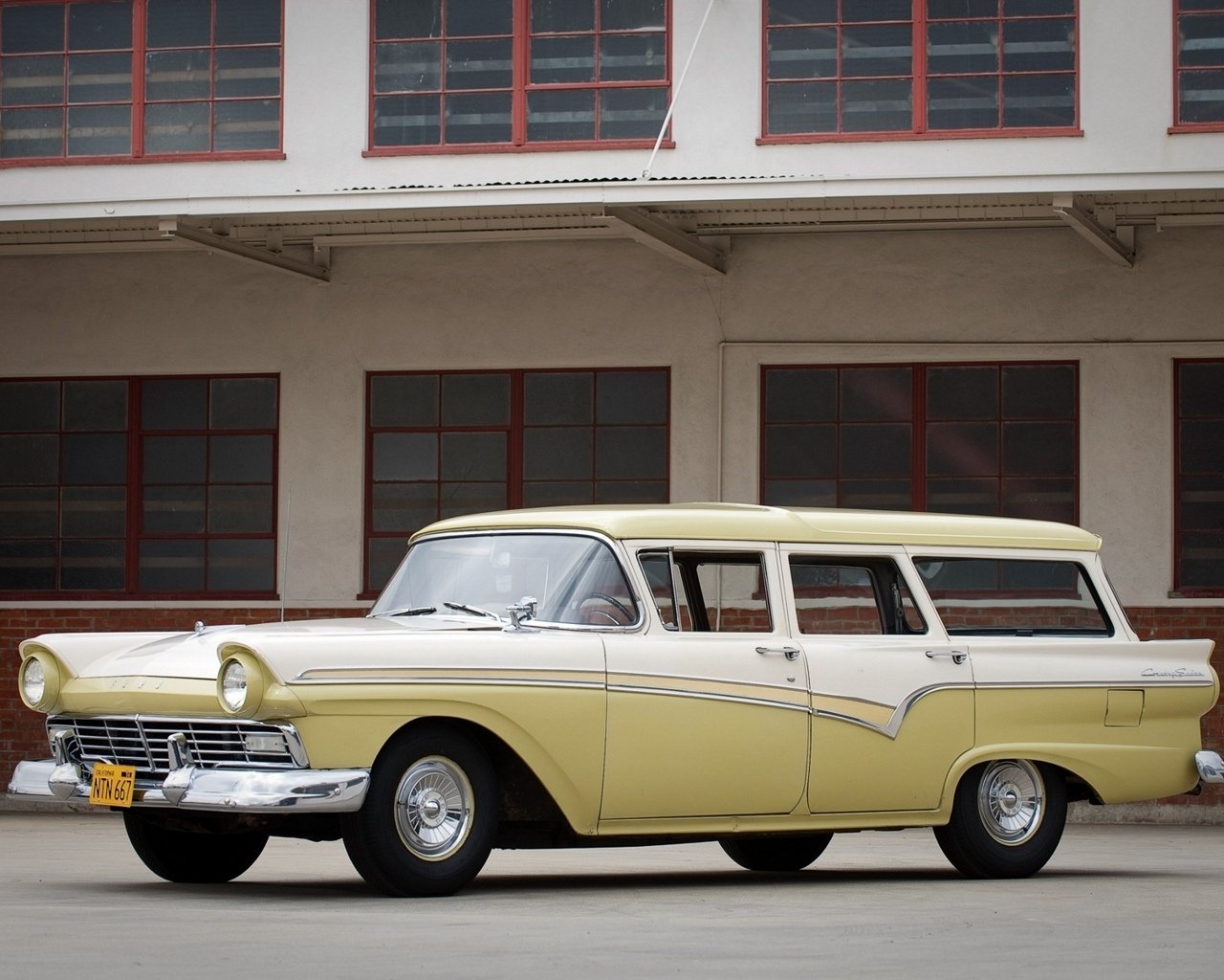Classic pale yellow-and-white Ford Country Sedan vehicle, a vintage station wagon, parked in front of an industrial building.