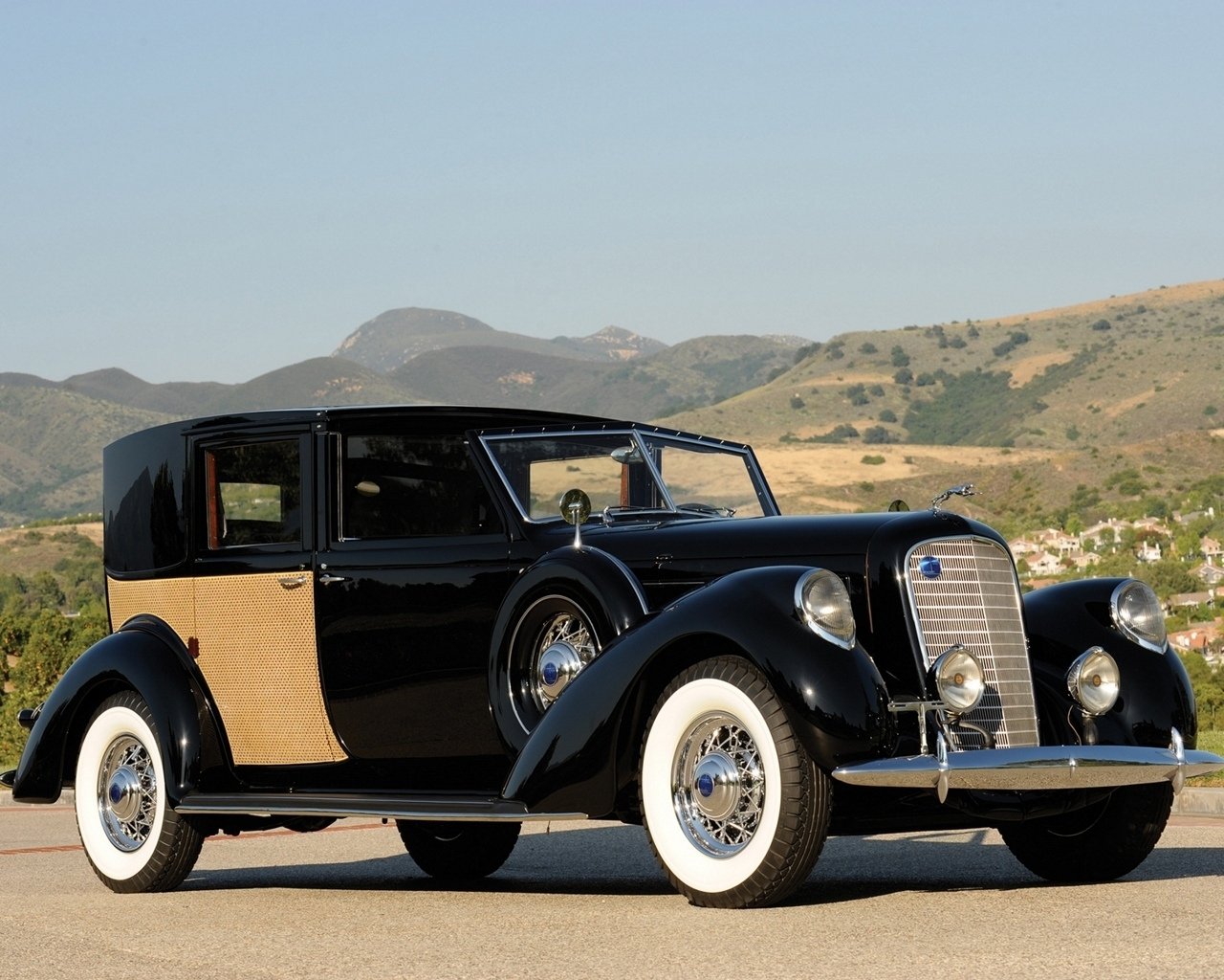 A classic black Lincoln K Panel Brougham with wood paneling, set against a mountainous backdrop under a clear sky.