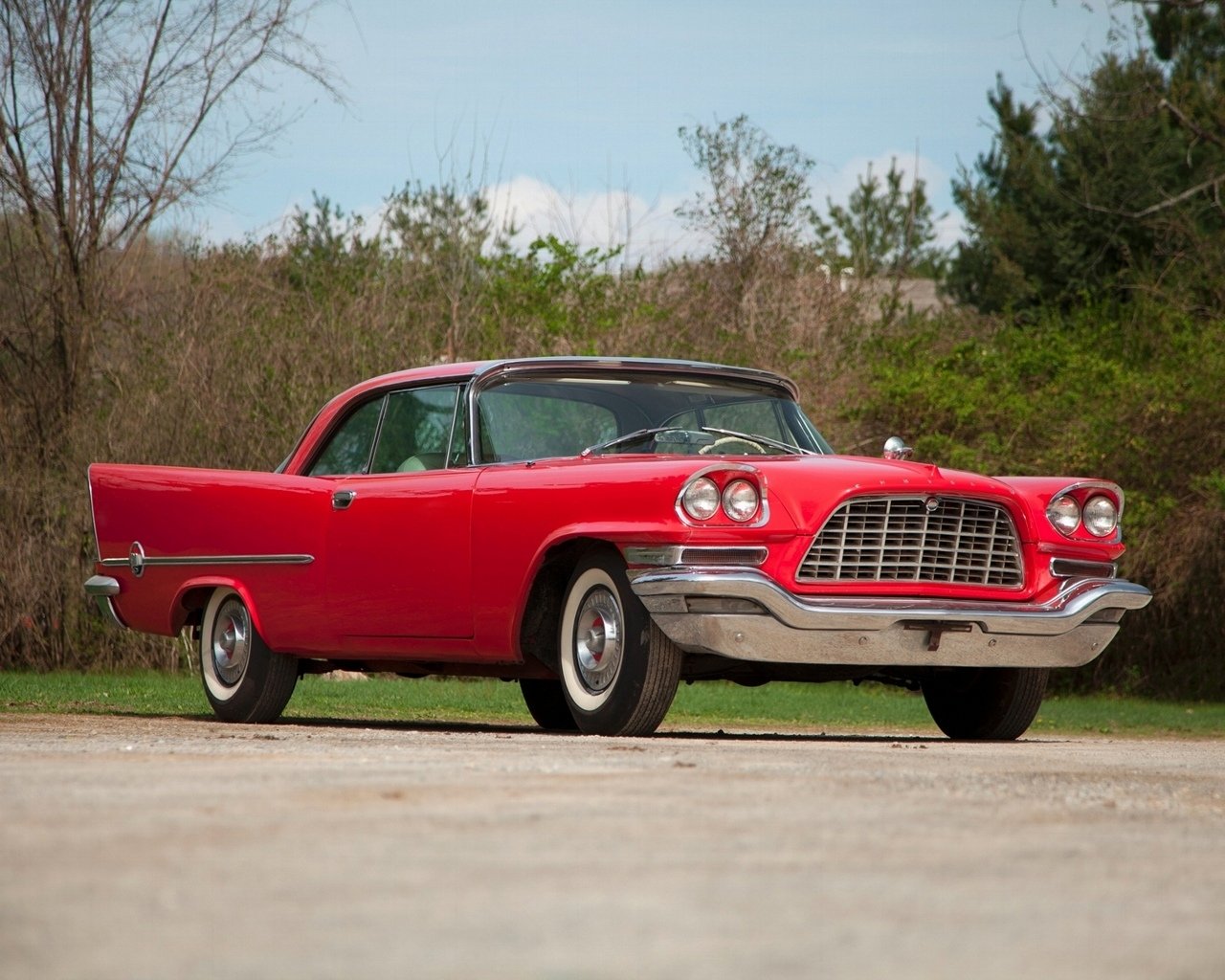 Classic vehicle — a red two-door coupe with a chrome grille, whitewall tires and sleek rear fins parked on a country road.