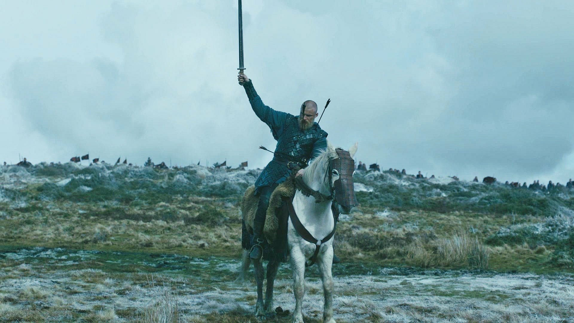 Scene from the TV show Vikings (2013): a lone warrior on a white horse raises a sword over a windswept, frosty shoreline under heavy, stormy skies.