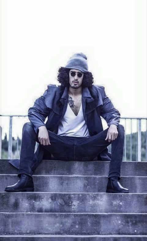 A stylish individual showcases a confident pose while seated on steps, wearing sunglasses and a hat, embodying a vibe reminiscent of characters from the anime One Piece.