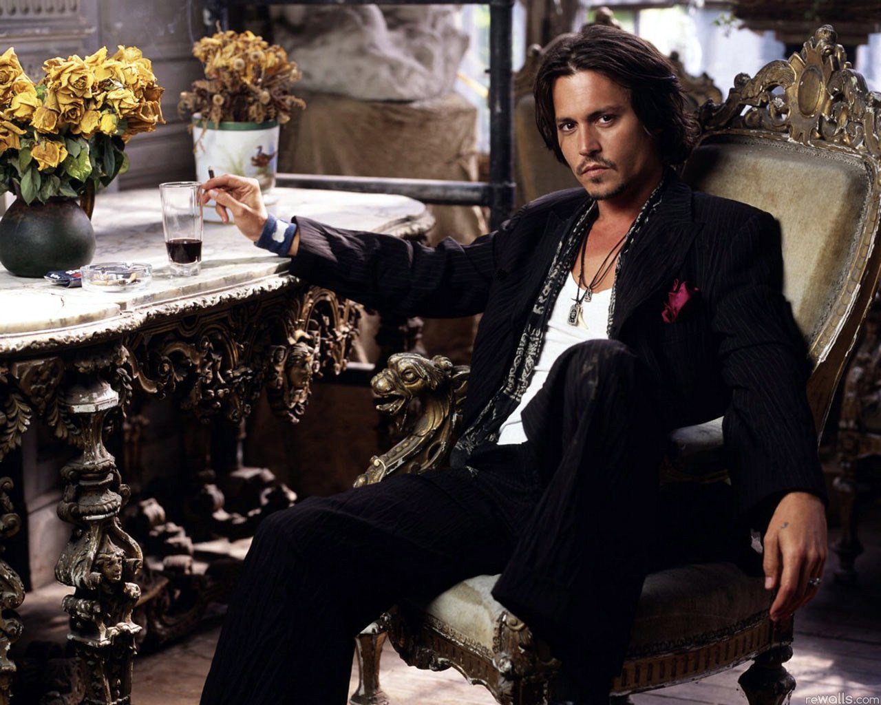 Johnny Depp sits confidently in an ornate chair, holding a drink, surrounded by eclectic decor and vibrant flowers, embodying a stylish and relaxed atmosphere.