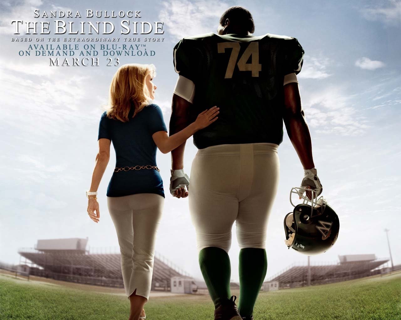 Movie poster for The Blind Side: a woman walks arm-in-arm with a towering football player wearing #74 across the stadium turf under a wide sky.
