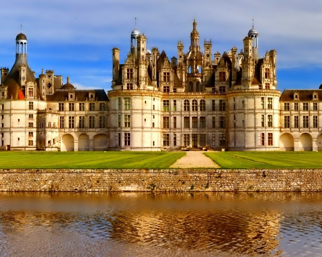 The image captures the majestic Château de Chambord, showcasing its intricate architecture reflected in the tranquil waters nearby. A stunning example of man-made beauty.
