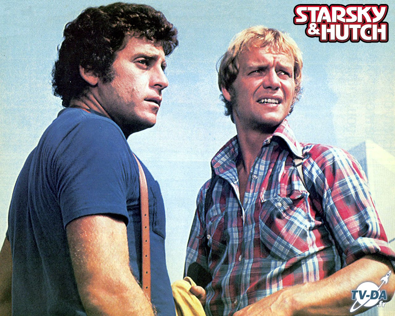 Promotional image for the TV show Starsky & Hutch: two detectives stand side by side, one in a blue tee and the other in a red plaid shirt, 1970s style.