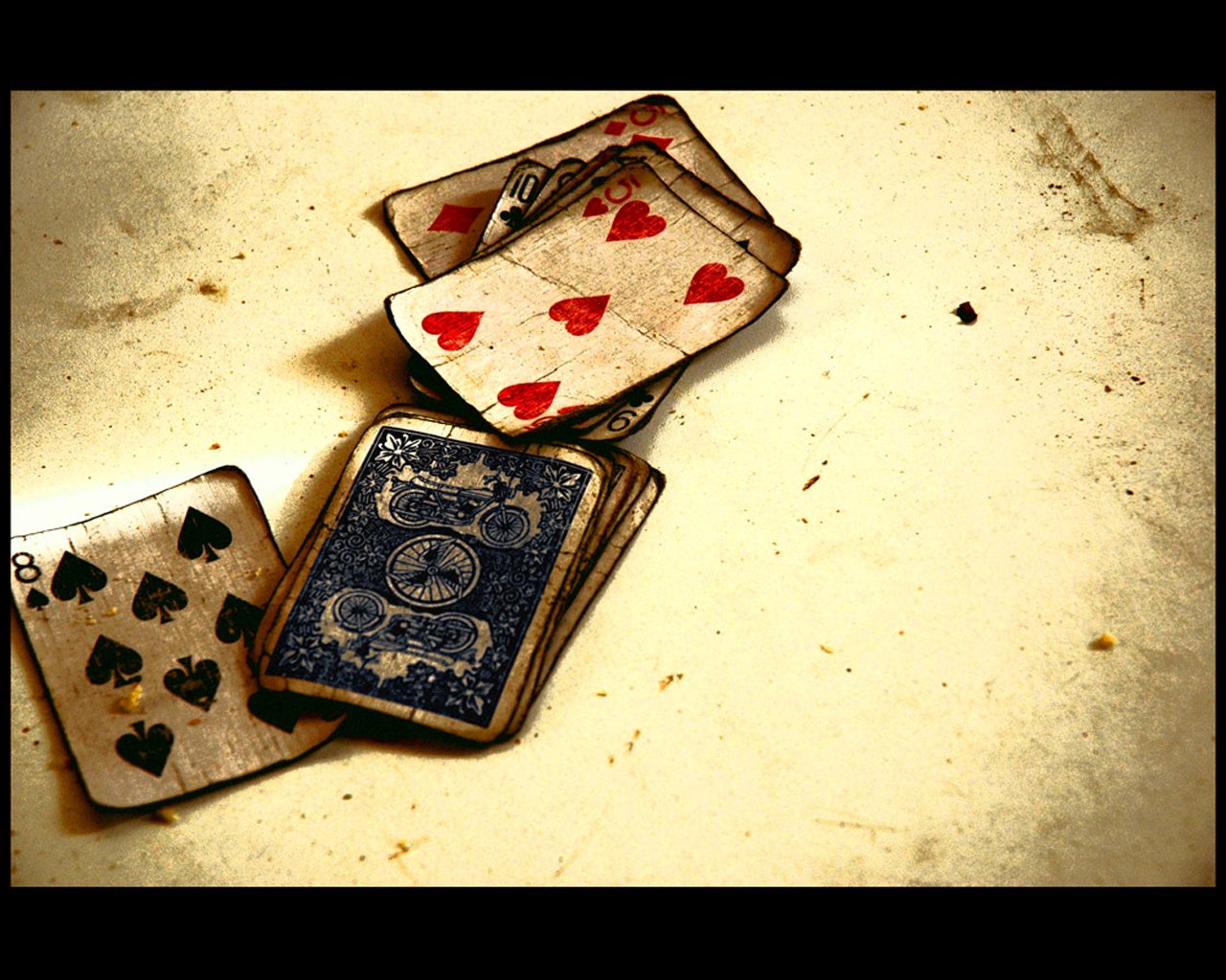 A scattered deck of worn playing cards featuring hearts and spades rests on a textured surface, showcasing the intricacies of man-made design.