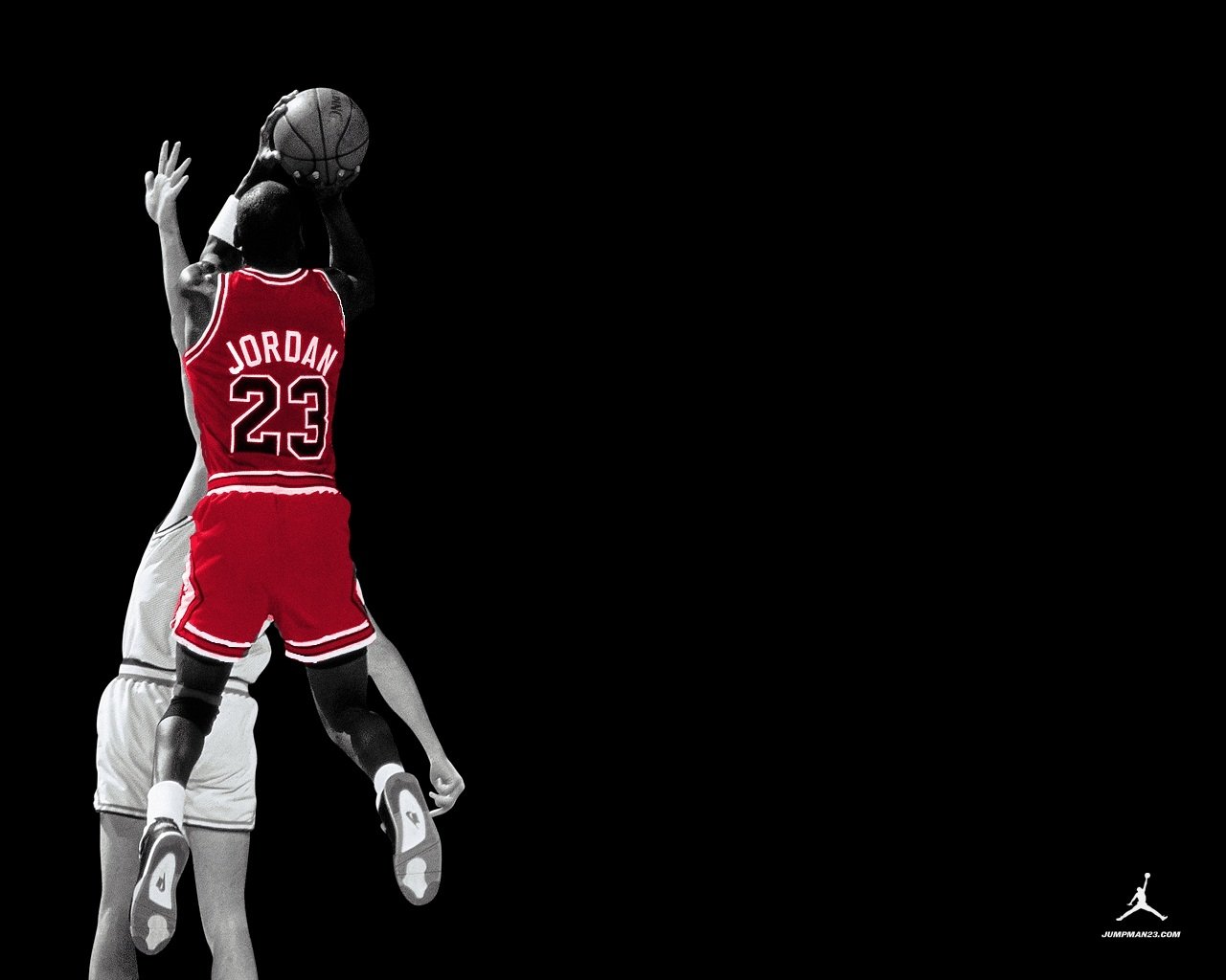 Michael Jordan, wearing his iconic red Chicago Bulls jersey, leaps to make a dynamic shot against an opponent, capturing the intensity of basketball sports.