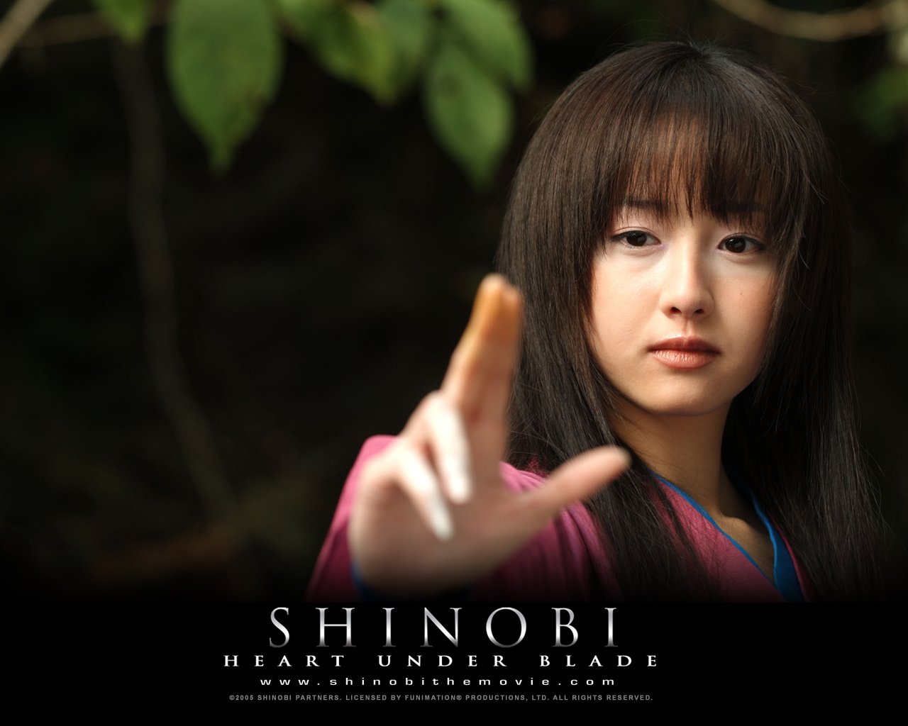 A young woman in traditional attire extends her hand forward in a scene from the movie Shinobi: Heart Under Blade with a natural, forested background.
