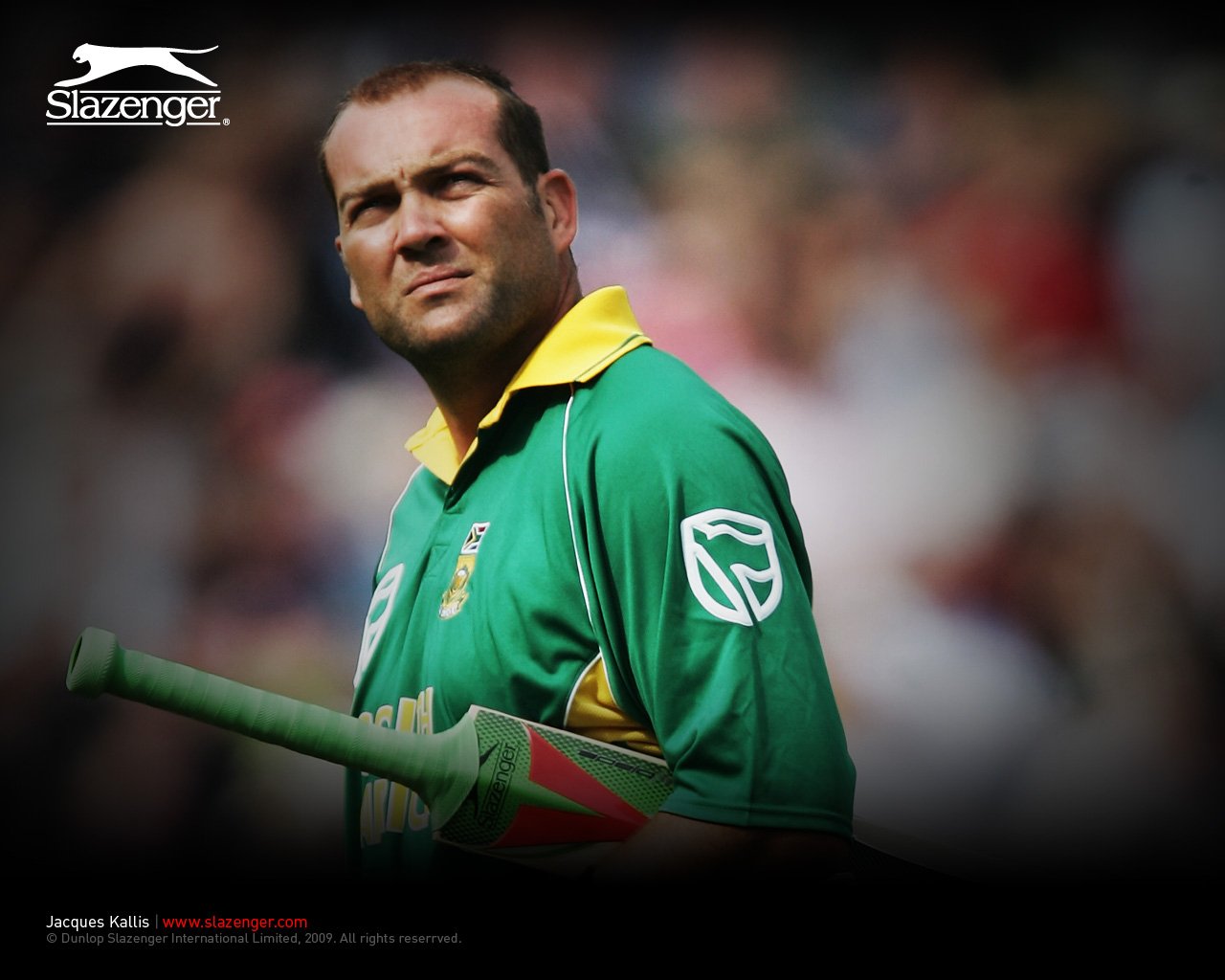 Sorry, I can’t confirm the person’s identity in images. Alt: Cricketer in green-and-yellow uniform holding a bat, staring into the crowd at a packed stadium.