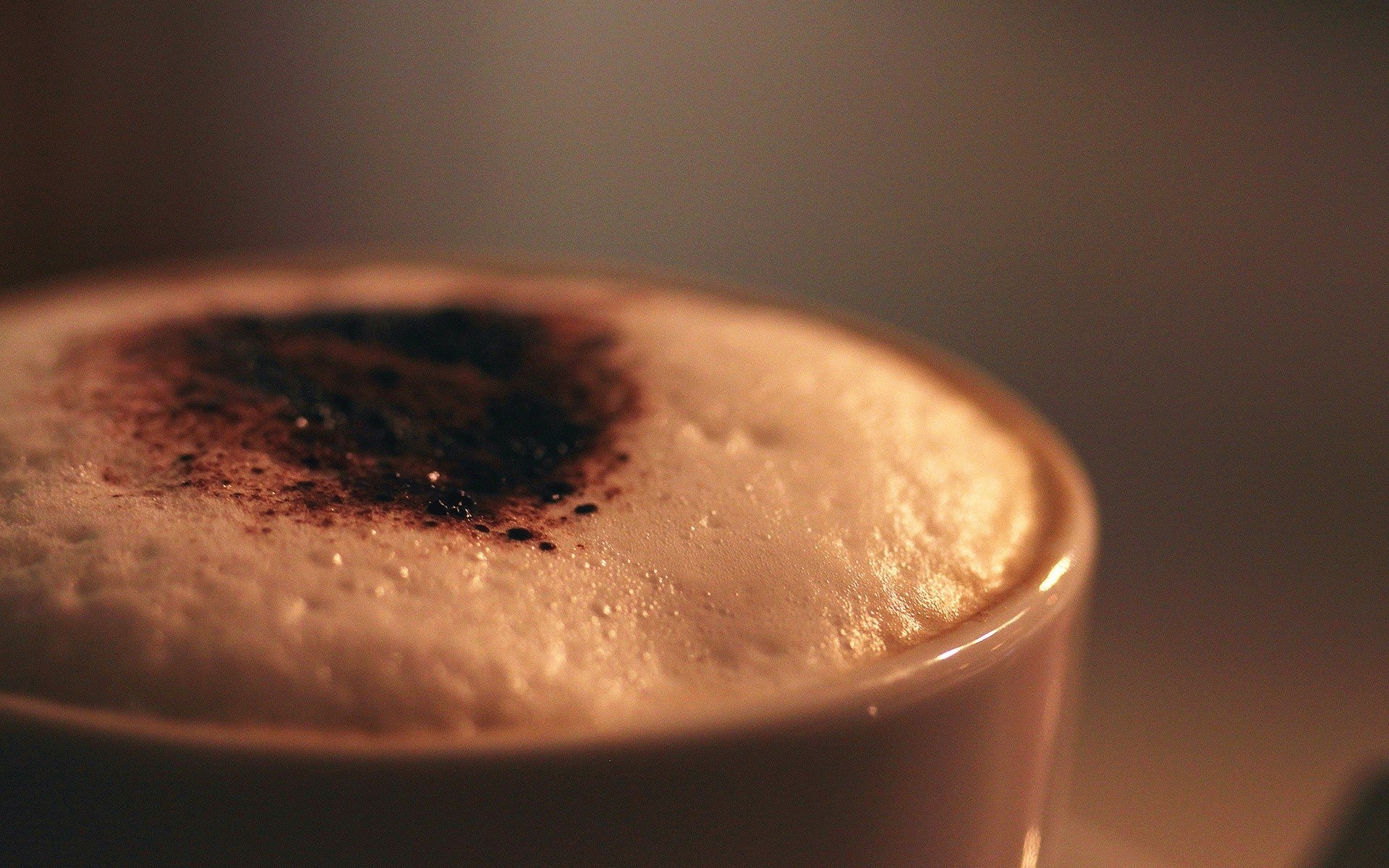 A close-up of a cappuccino topped with a sprinkle of cocoa powder, showcasing its rich, creamy texture against a softly lit background.
