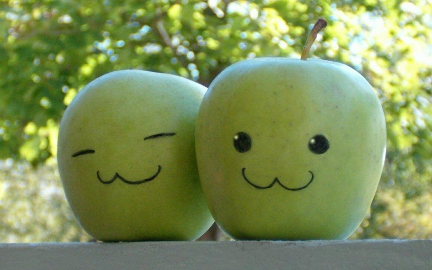 Two cheerful green apples with cute, smiling faces sit side by side against a blurred natural background, showcasing their playful and friendly expressions.
